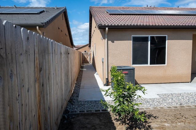 view of home's exterior featuring a tile roof, stucco siding, fence, and solar panels