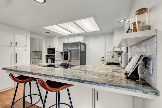 kitchen with light stone counters, a sink, washer and dryer, black appliances, and a peninsula