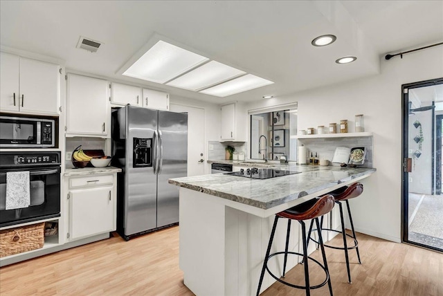 kitchen with black appliances, white cabinetry, light wood finished floors, and visible vents