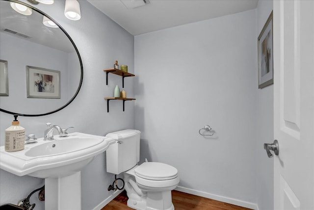 half bath featuring a sink, wood finished floors, baseboards, toilet, and visible vents