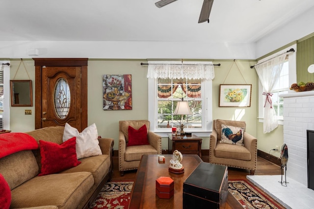 living area featuring a brick fireplace, wood finished floors, and a ceiling fan