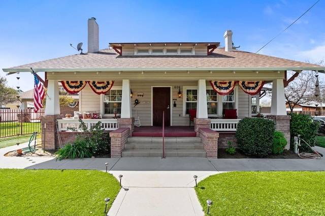 view of front facade featuring fence, a chimney, a front yard, a shingled roof, and a porch