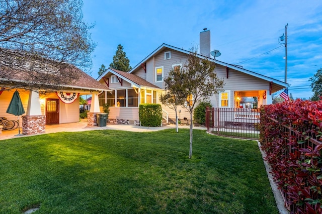 back of property featuring a chimney, fence, a sunroom, a patio, and a lawn