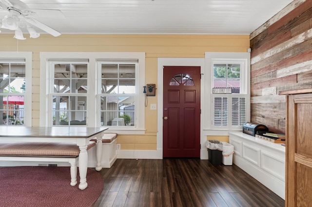 foyer entrance with dark wood-style floors, wooden walls, and a ceiling fan