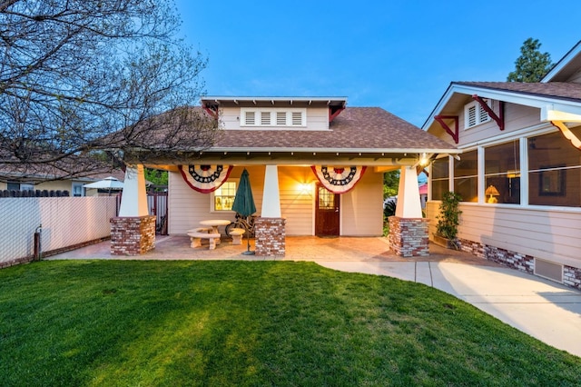 rear view of property featuring a patio area, a shingled roof, fence, and a lawn