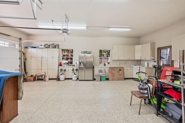 garage with a garage door opener, stainless steel fridge, and a sink