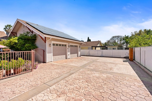 garage with roof mounted solar panels, a gate, and fence