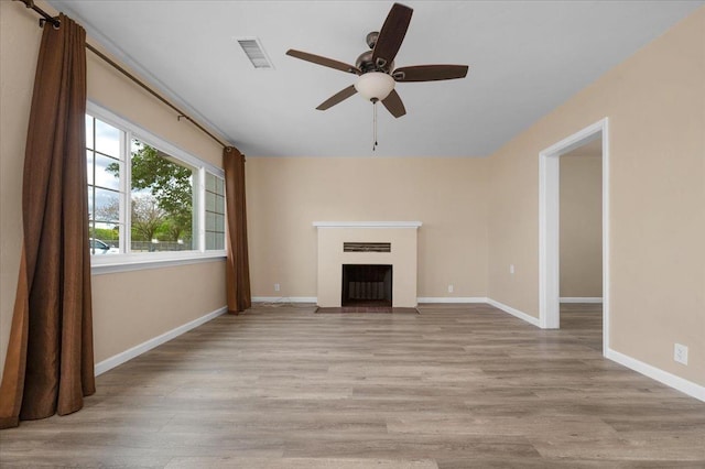 unfurnished living room with a fireplace with flush hearth, baseboards, ceiling fan, visible vents, and wood finished floors