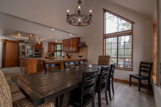 dining space with baseboards, a raised ceiling, a chandelier, recessed lighting, and light wood finished floors