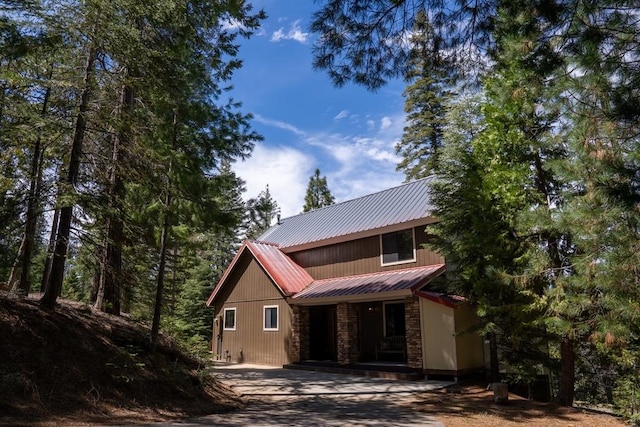 view of front of house featuring driveway, metal roof, and stone siding