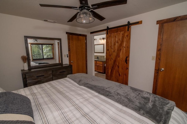 bedroom featuring a barn door, visible vents, ensuite bath, and ceiling fan