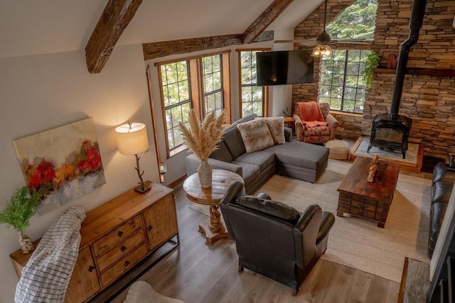living room featuring wood finished floors, a wood stove, lofted ceiling with beams, and plenty of natural light