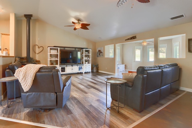 living room featuring vaulted ceiling, wood finished floors, a wood stove, visible vents, and ceiling fan