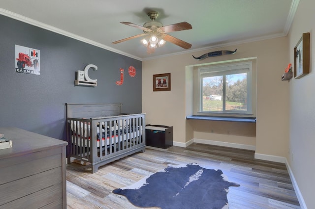 bedroom featuring baseboards, ornamental molding, wood finished floors, and a nursery area