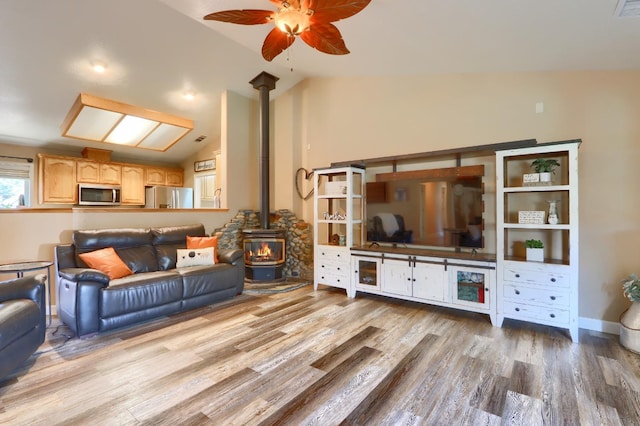 living area with baseboards, wood finished floors, a ceiling fan, a wood stove, and vaulted ceiling