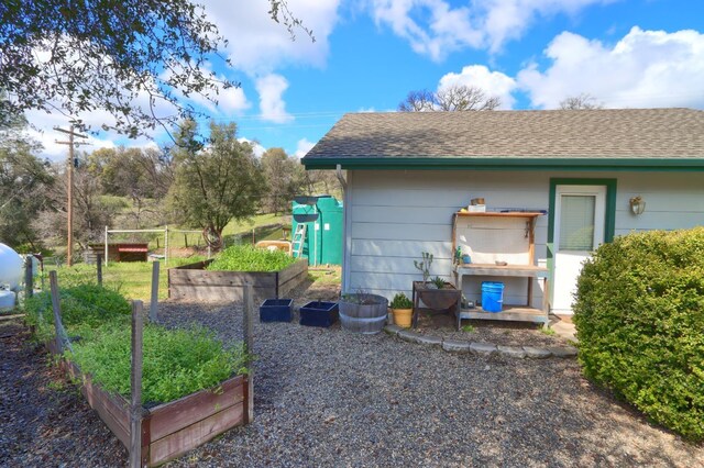exterior space with roof with shingles, fence, and a vegetable garden