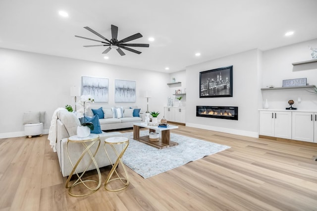 living room featuring a glass covered fireplace, recessed lighting, light wood finished floors, and ceiling fan