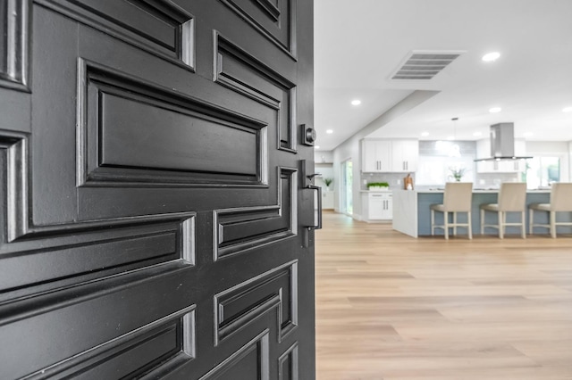 room details featuring range hood, visible vents, light wood-style floors, white cabinetry, and recessed lighting