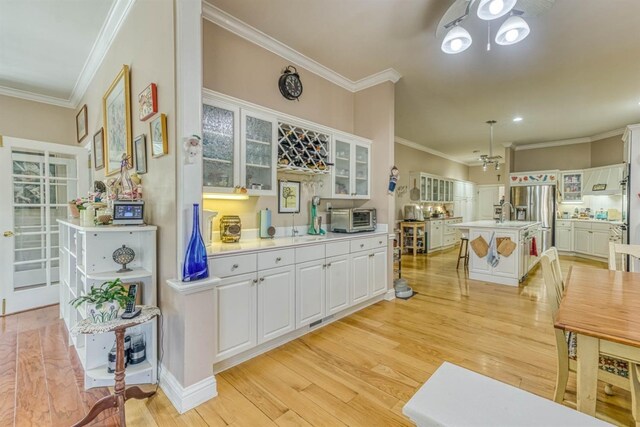 49521 Stillmeadow Dr, Oakhurst, CA 93644 - kitchen with glass insert cabinets, light countertops, white cabinetry, crown molding, and light wood finished floors