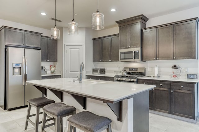 kitchen featuring stainless steel appliances, a sink, dark brown cabinetry, a kitchen bar, and light tile patterned floors