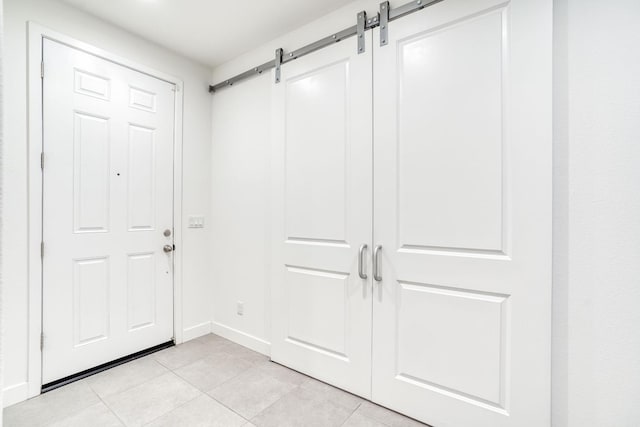 foyer entrance featuring light tile patterned flooring, a barn door, and baseboards