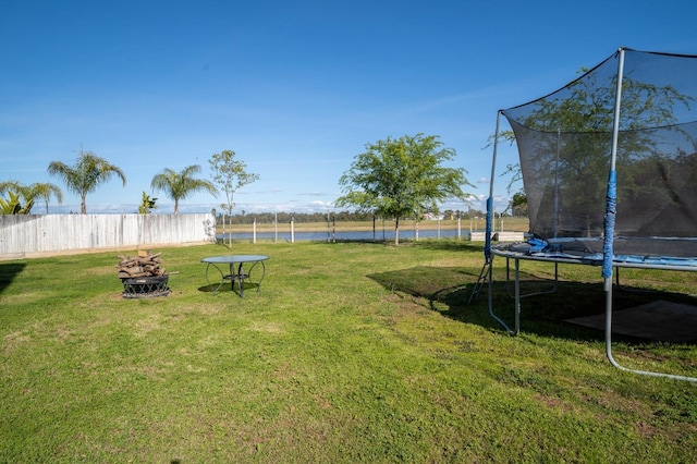 view of yard with fence, a trampoline, a water view, and an outdoor fire pit