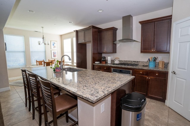 kitchen with a sink, a kitchen bar, light stone counters, wall chimney range hood, and appliances with stainless steel finishes