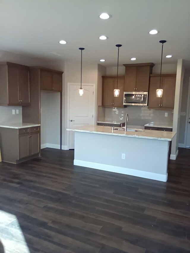 15956 W Dylan Ave, Kerman, CA 93630 - kitchen with stainless steel microwave, dark wood-style flooring, decorative light fixtures, a center island with sink, and a sink