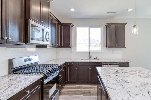 kitchen featuring tasteful backsplash, a sink, appliances with stainless steel finishes, dark brown cabinetry, and light stone countertops