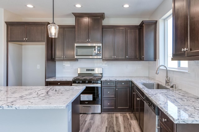 kitchen featuring light wood-style flooring, dark brown cabinets, light stone counters, a sink, and stainless steel appliances