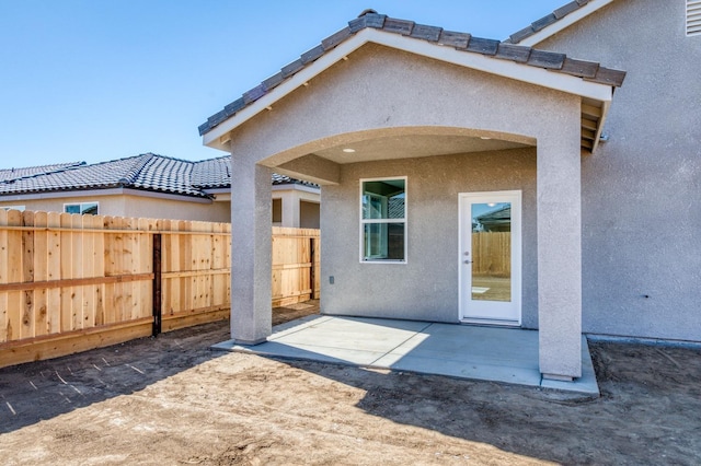 rear view of house featuring a tiled roof, a patio area, stucco siding, and fence