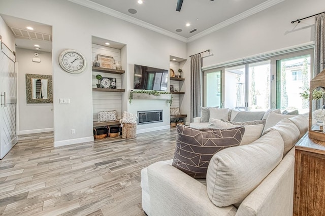living room featuring visible vents, baseboards, ornamental molding, light wood-style floors, and a glass covered fireplace