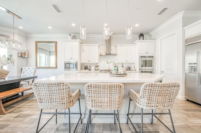 kitchen with tasteful backsplash, wall chimney range hood, built in appliances, and visible vents