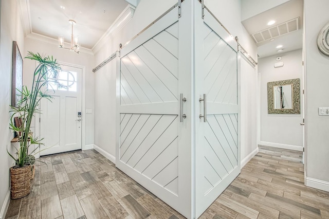 interior space featuring a barn door, visible vents, crown molding, and wood finished floors