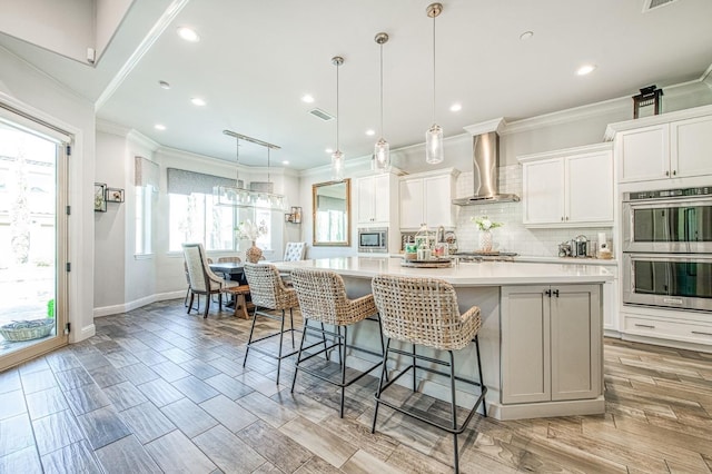kitchen with wall chimney exhaust hood, appliances with stainless steel finishes, light countertops, decorative backsplash, and a spacious island