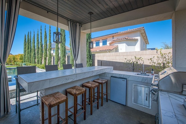 view of patio / terrace with area for grilling, an outdoor kitchen, fence, and outdoor wet bar