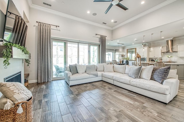 living area featuring light wood finished floors, visible vents, ornamental molding, and ceiling fan