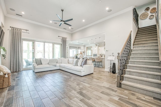 living area with visible vents, a ceiling fan, light wood-style floors, crown molding, and stairs