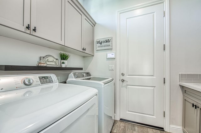 clothes washing area with light wood-style flooring, cabinet space, and washing machine and dryer