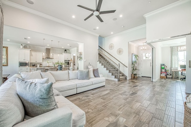 living room with baseboards, ornamental molding, ceiling fan with notable chandelier, stairs, and light wood-style flooring