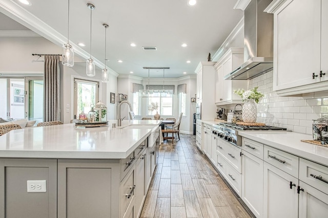 kitchen featuring tasteful backsplash, visible vents, wall chimney exhaust hood, light countertops, and stainless steel gas stovetop