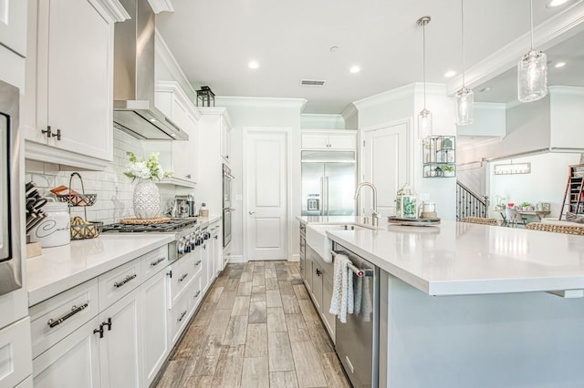 kitchen featuring stainless steel appliances, a sink, crown molding, and wall chimney range hood