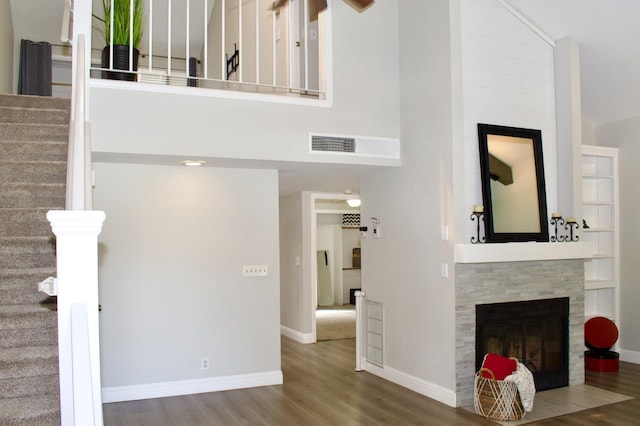 unfurnished living room with stairway, visible vents, baseboards, a tile fireplace, and wood finished floors