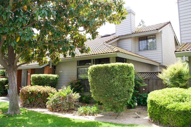 view of side of home with a chimney, fence, and a tile roof