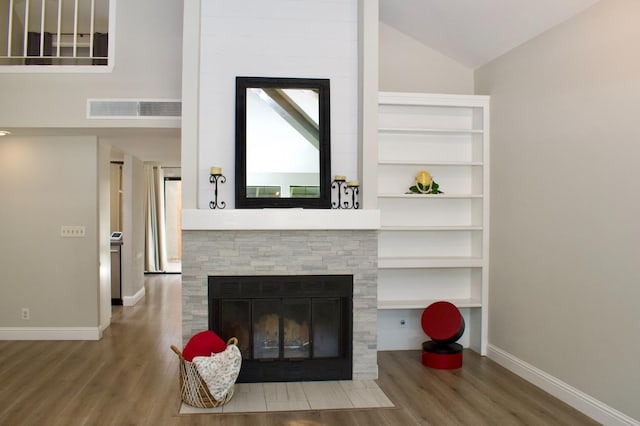 living area with a fireplace, visible vents, vaulted ceiling, baseboards, and wood finished floors