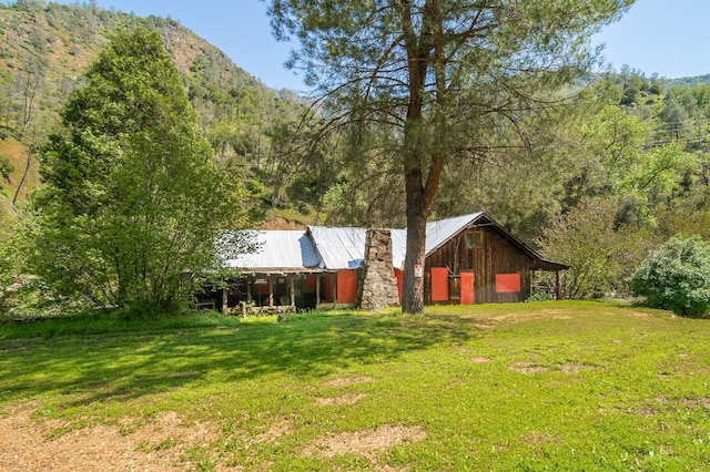 rear view of house with a wooded view, an outdoor structure, metal roof, and a lawn