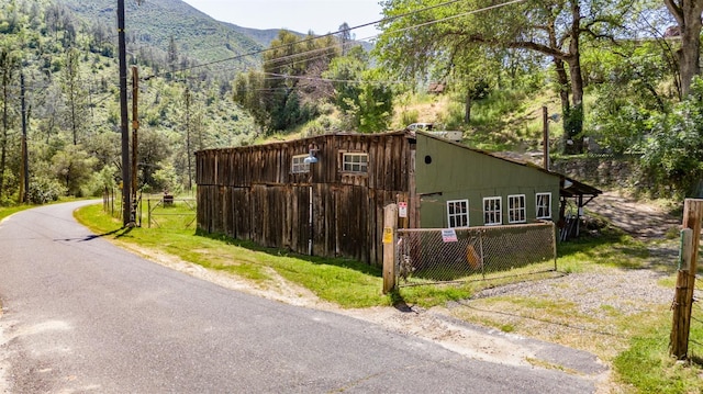 view of property exterior with a wooded view, a mountain view, and fence