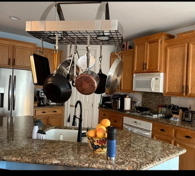 1068 San Ramon Ave, Madera, CA 93637 - kitchen featuring a sink, white appliances, brown cabinetry, dark stone counters, and decorative backsplash