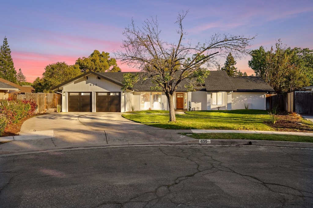ranch-style home featuring a yard, an attached garage, fence, and driveway