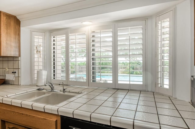 kitchen featuring brown cabinets, tile countertops, a sink, and backsplash